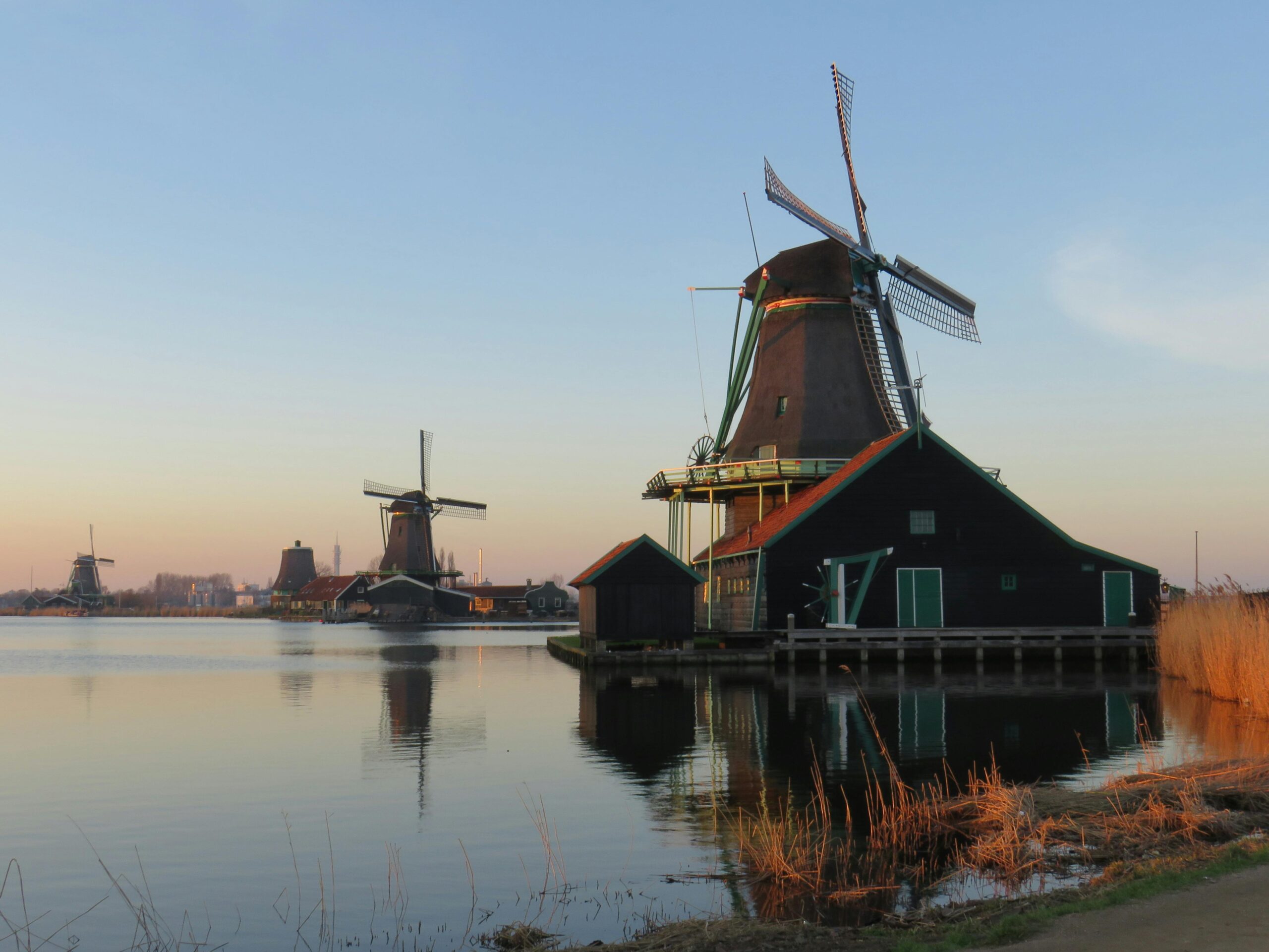 Scenic view of traditional Dutch windmills reflecting on the water during twilight in Amsterdam.