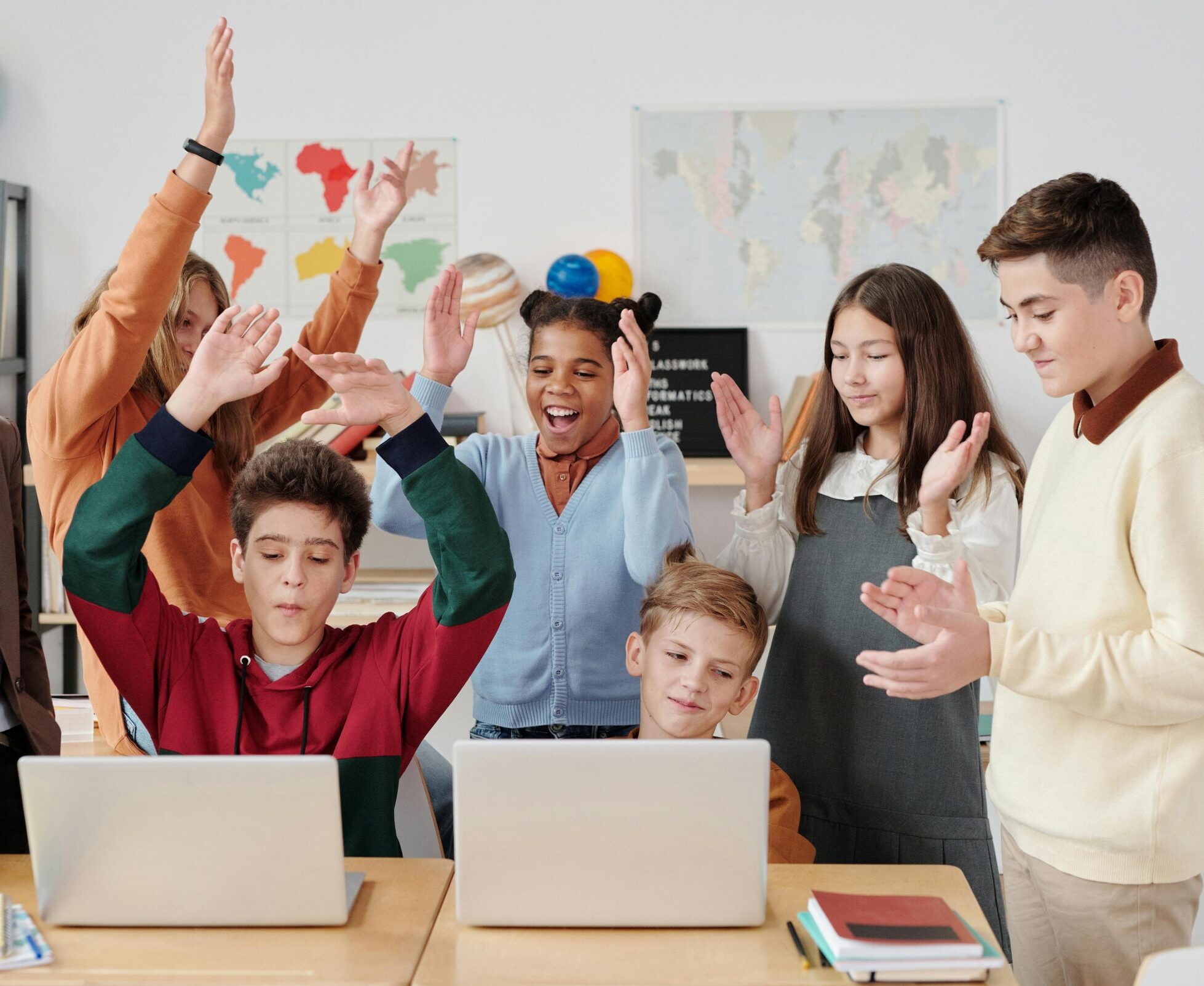 A group of happy students and a teacher clapping together in a school classroom.