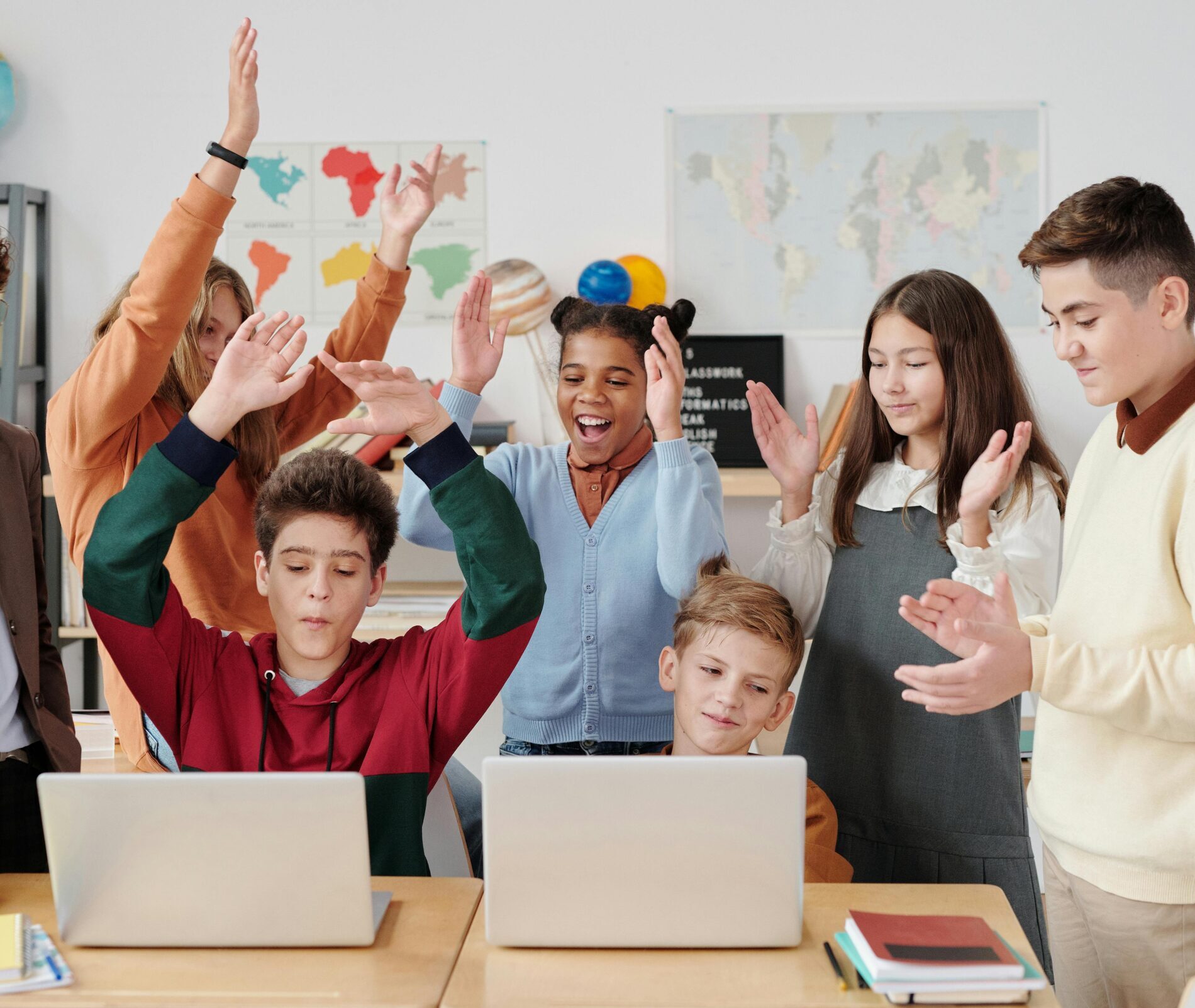 A group of happy students and a teacher clapping together in a school classroom.